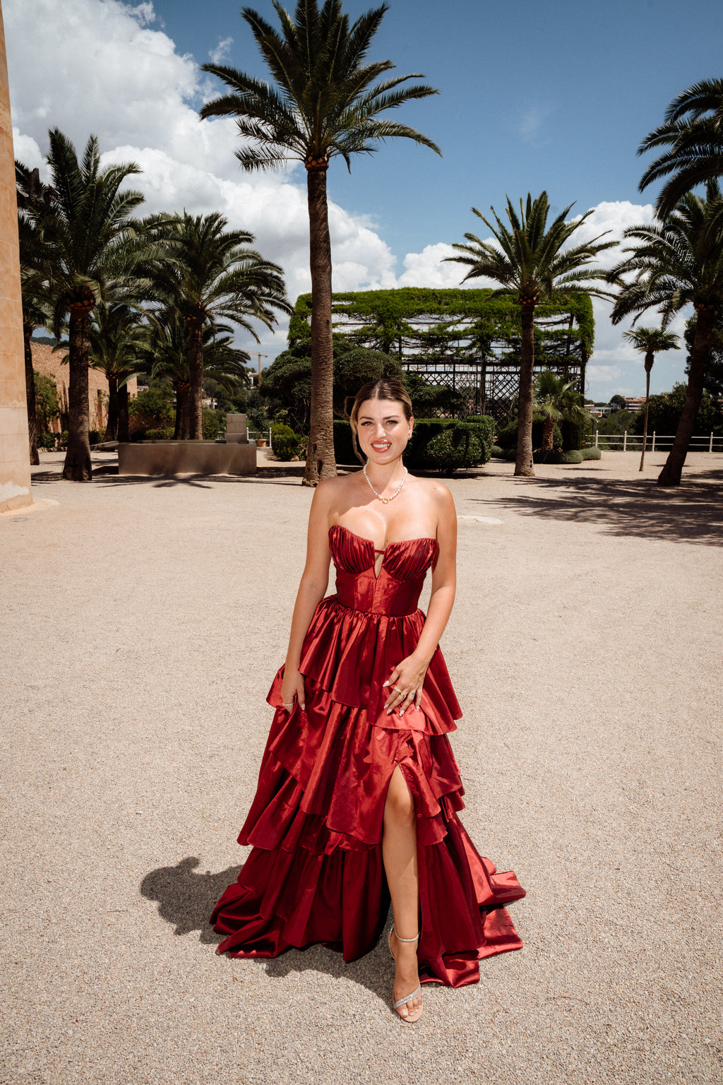 Frau in rotem Abendkleid mit Beinschlitz zwischen Palmen, Editorial-Porträt bei Hochzeit