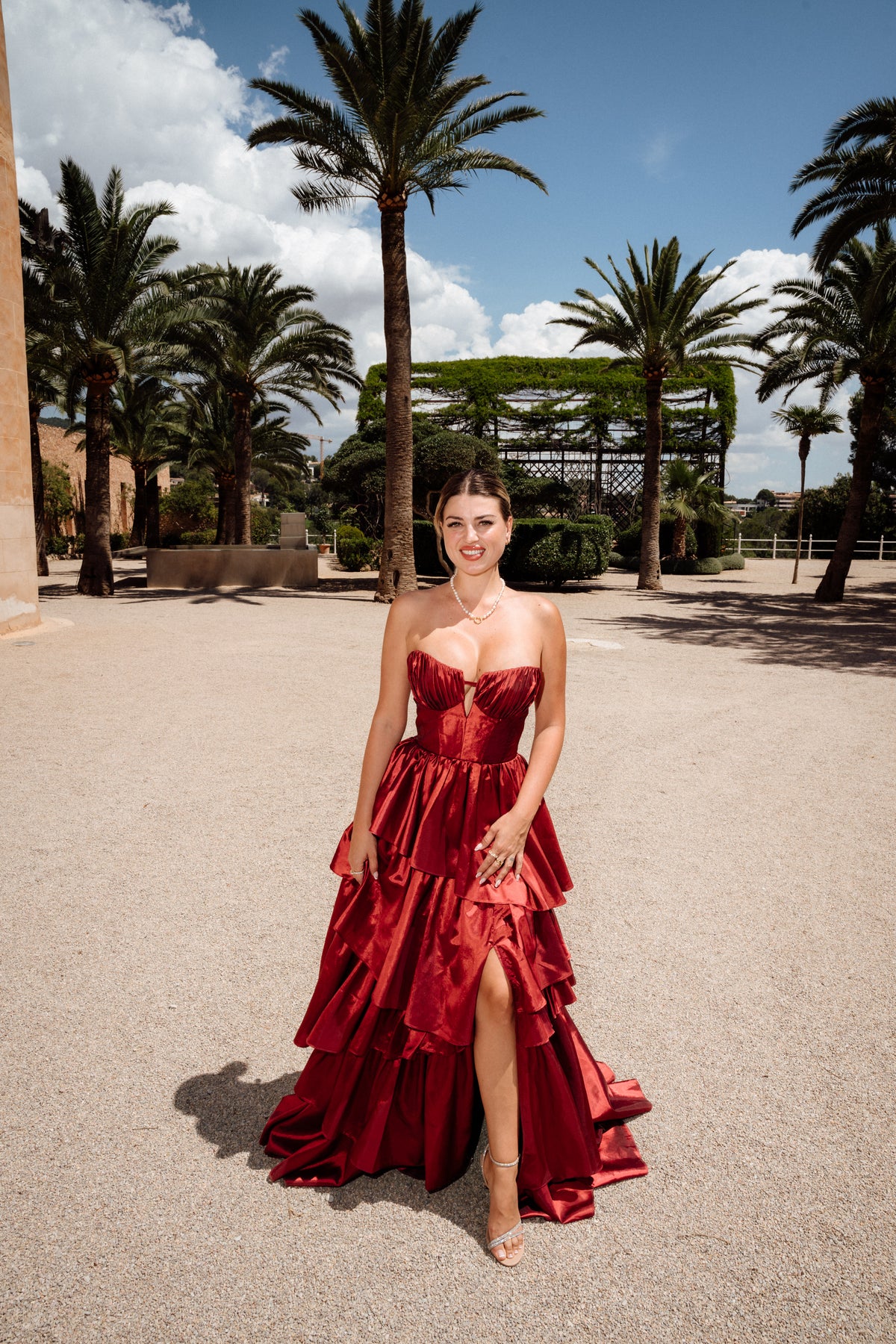Frau in rotem Abendkleid mit Beinschlitz zwischen Palmen, Editorial-Porträt bei Hochzeit